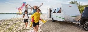 blije familie bij auto en caravan op het strand